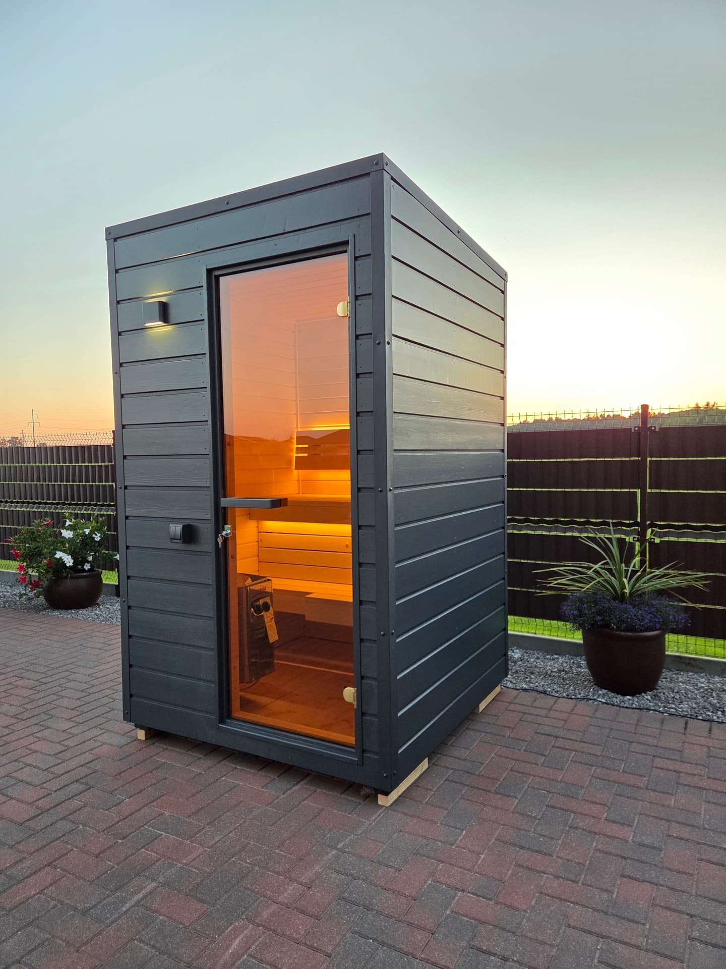 The cabin at sunset with the sun low behind the fence and the interior lit